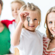 Eine Familie vor einem weißen Hintergrund lächelt, ein Mädchen hält einen Schlüssel in der Hand - Immobilienkauf