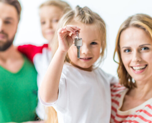 Eine Familie vor einem weißen Hintergrund lächelt, ein Mädchen hält einen Schlüssel in der Hand - Immobilienkauf