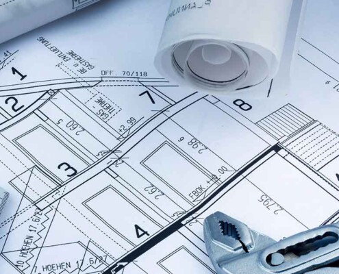 Grundrissplan eines Hauses, darauf liegen ein Zollstock, eine Rohrzange, ein Taschenrechner und gerollte Baupläne | Barrierefreier Umbau