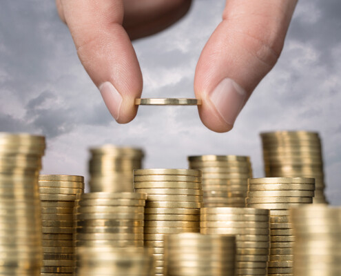 Savings, close up of male hand stacking golden coins over sky ba; Preisanstieg beim Bauen