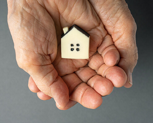 Inheritance concept. Elderly woman hands holds a little toy house. Inherited property idea; Erbschaftssteuer