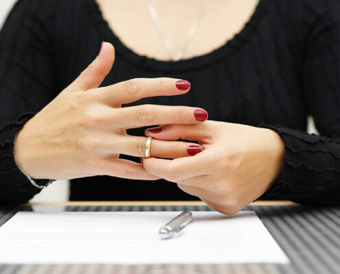 Eine Frau die Ihren Ehering vom Finger zieht - Scheidungsimmobilie