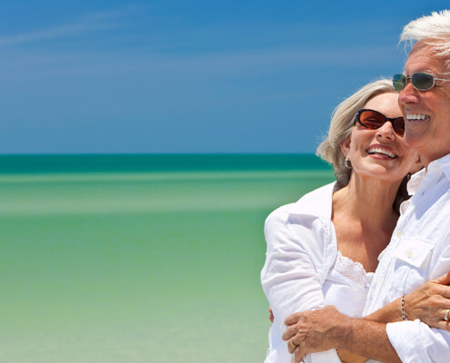 Ein älteres Paar mit Sonnenbrille vor einem blauen Himmer und Meer - Wohnen im Alter