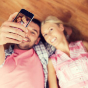 Ein junges Paar liegt glücklich auf dem Fußboden in seiner neu gekauften Immobilie und macht ein Selfie | Immobilienkauf