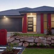Haus mit Garageneinfahrt, kleinem Mäuerchen und Rasen im Vorgarten mit Licht bei Abenddämmerung | Notverkauf
