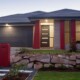 Haus mit Garageneinfahrt, kleinem Mäuerchen und Rasen im Vorgarten mit Licht bei Abenddämmerung | Notverkauf