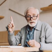 Alter Mann sitzt im Café am Laptop, surft im Internet und hebt den Zeigefinger und macht große Augen, weil er eine Idee hat.