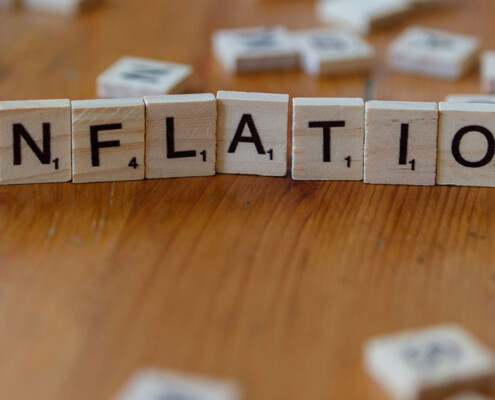 Auf einem Tisch liegt aus Scrabble-Buchstaben gelegt das Wort "Inflation" als Symbol für Immobilieninvestments während einer Inflation | Immobilieninvestment