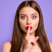 ein junge Frau, die sich den Zeigefinger vor den Mund hält um Verschwiegenheit zu demonstrieren