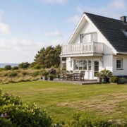 Ein weißes Ferienhaus mit Terrasse und großem Garten liegt in Küstennähe und steht sinnbildlich für den Verkauf einer nicht mehr passenden Ferienimmobilie. I Ferienimmobilie verkaufen