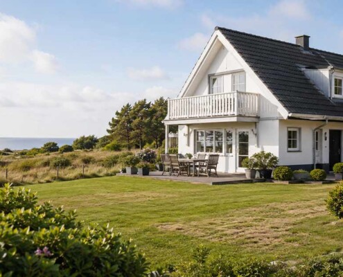 Ein weißes Ferienhaus mit Terrasse und großem Garten liegt in Küstennähe und steht sinnbildlich für den Verkauf einer nicht mehr passenden Ferienimmobilie. I Ferienimmobilie verkaufen